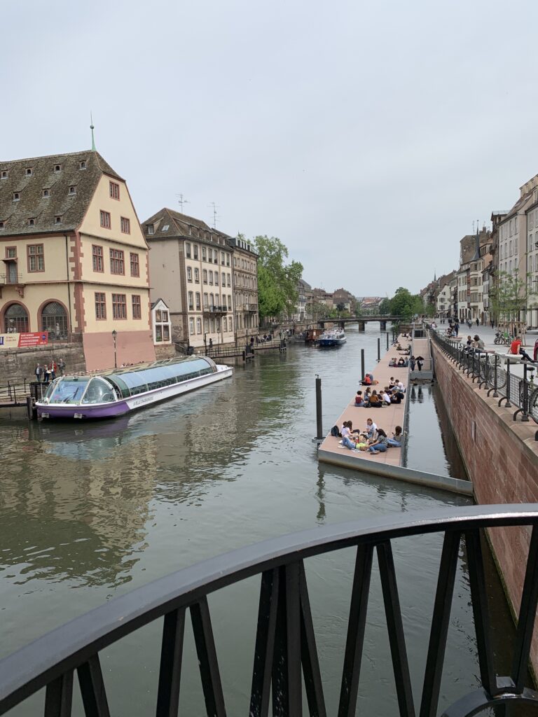 A canal on the edge of Strasbourg's old town. People enjoy picnics on a dock, and a tourist boat waits to load guests onboard.