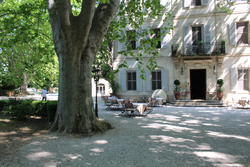 bistro tables sit in the shade in front of a large French Château in Provence