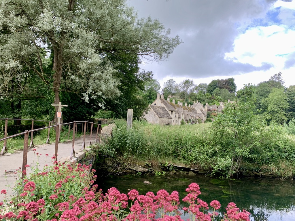 Flowers frame a picture of a bridge and the cottages in the Cotswold Village of Bibury, England