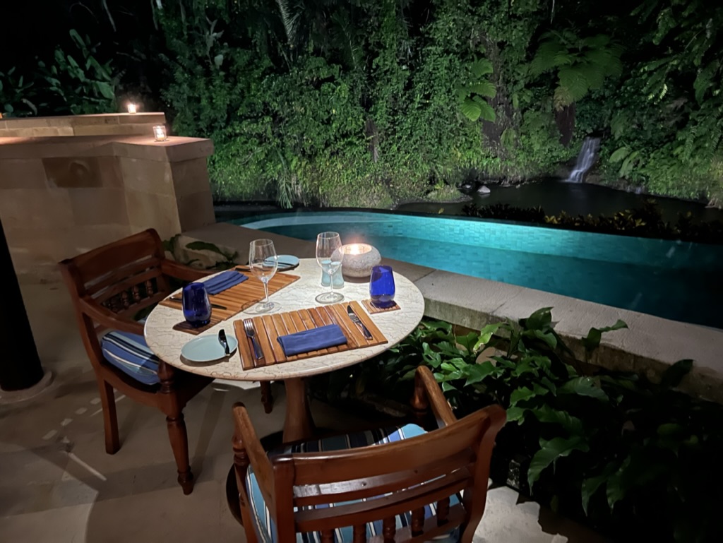 A beautiful two-top table sits overlooking a lit pool at night.