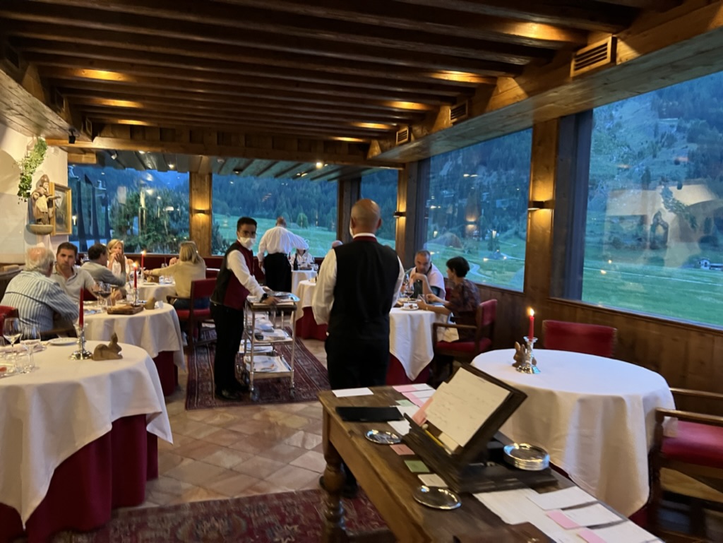 Alpine restaurant in Cogne, Italy at dusk. Waiters are serving tables with white-linens, while guests enjoy the view of the Italian mountains.