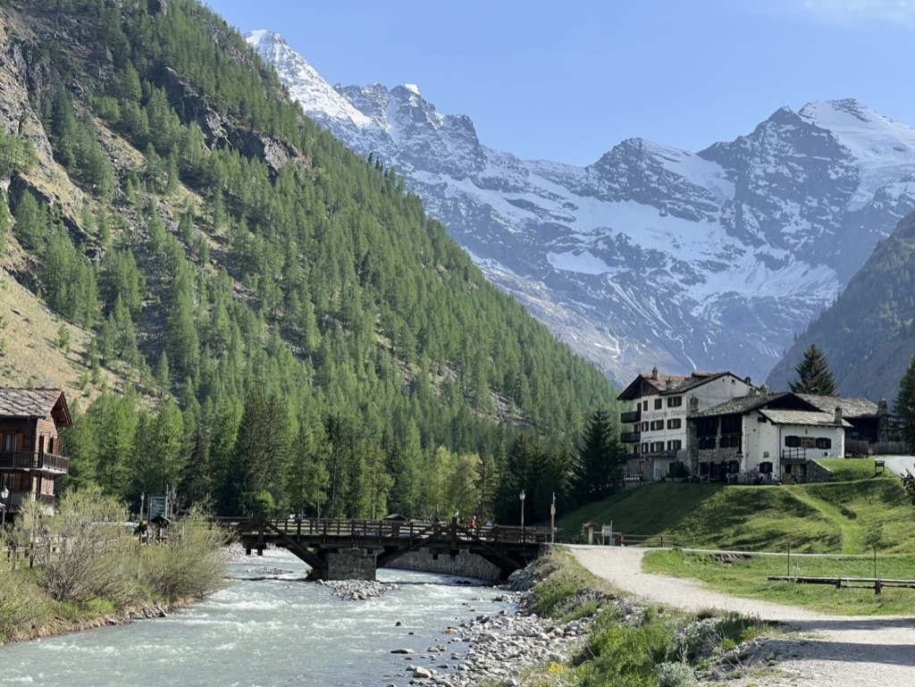 A glacial river sits in the foreground near a small village and steep mountains in the Grand Paradiso National Park in Italy.