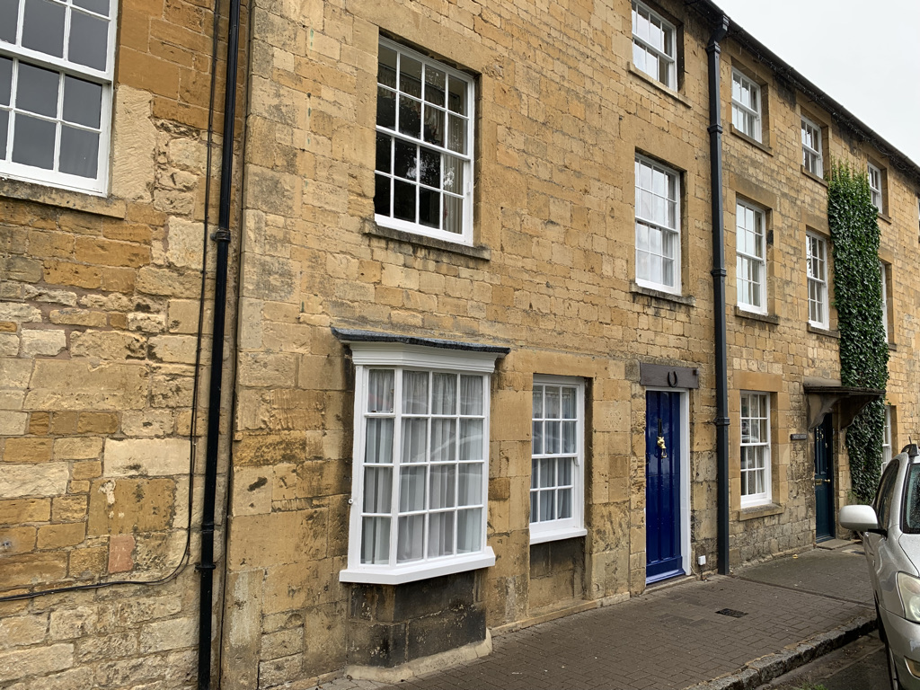 Stone row house in Chipping Campden, England. There is a bay window and a royal blue front door.