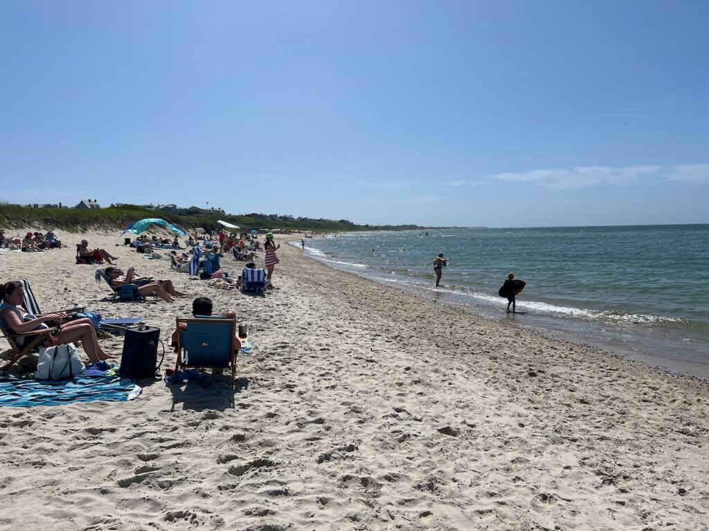 Clear blue sky day on the beach in Nantucket. Families sit and play on the sand.