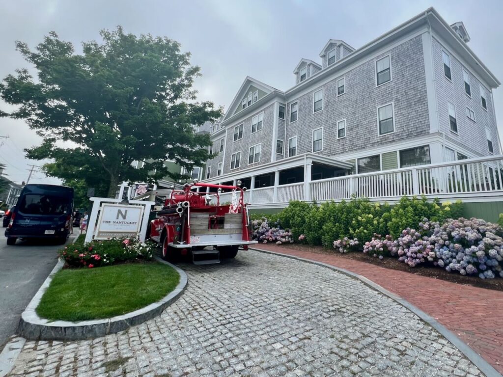 The Nantucket Hotel is a gray shingled hotel with two antique cars in front and blooming hydrangeas.