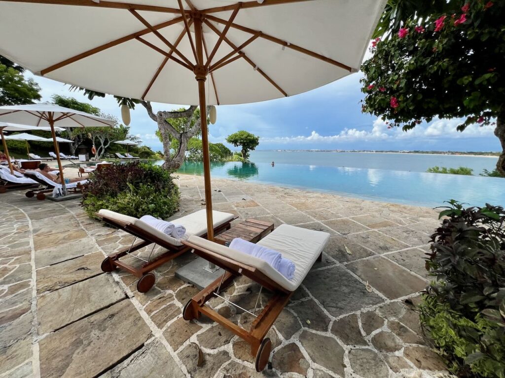 White cushioned lounge chairs by an infinity pool in Jimbaran Bay Bali